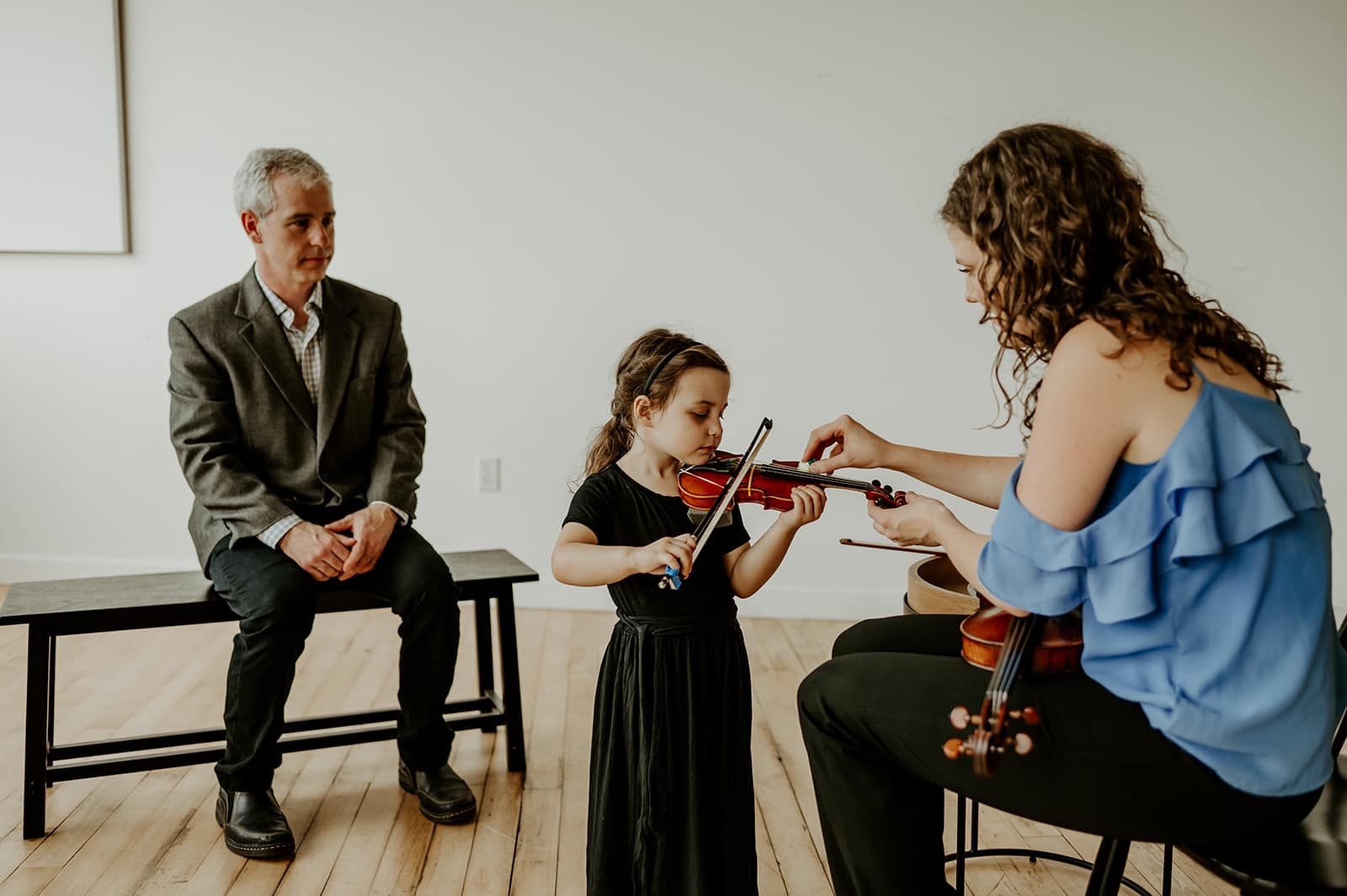 A woman is teaching a little girl how to play a violin.