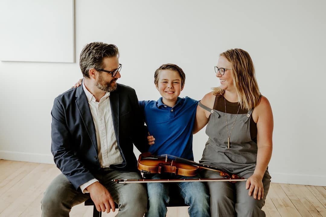 A man and a woman are sitting next to a boy holding a violin.