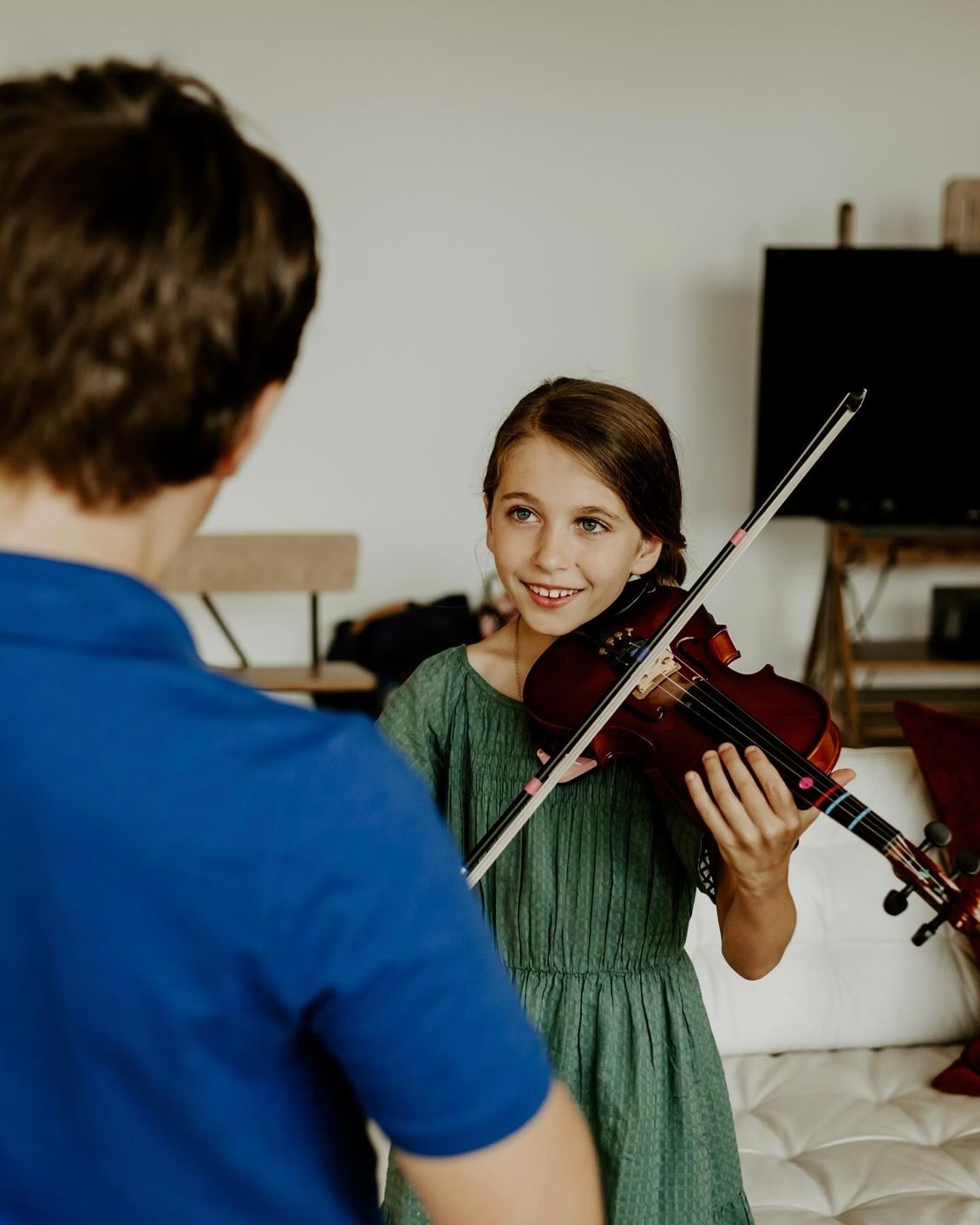 A young girl is playing a violin in front of a boy.