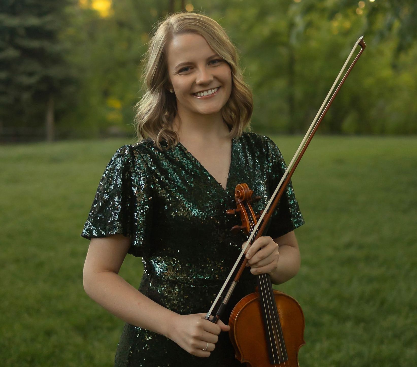 A woman is holding a violin in front of a window.