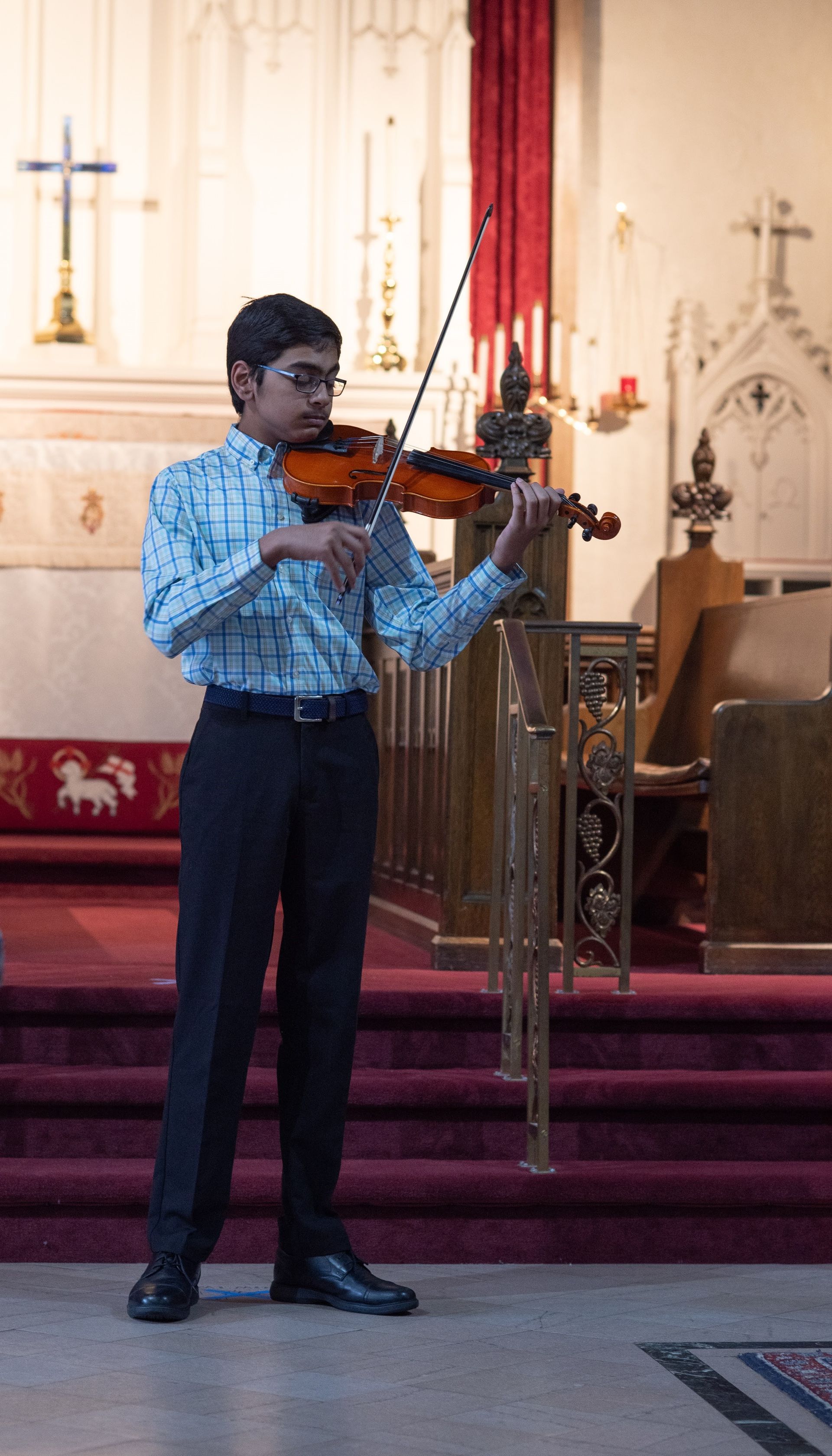 A young girl in a red shirt is playing a violin.