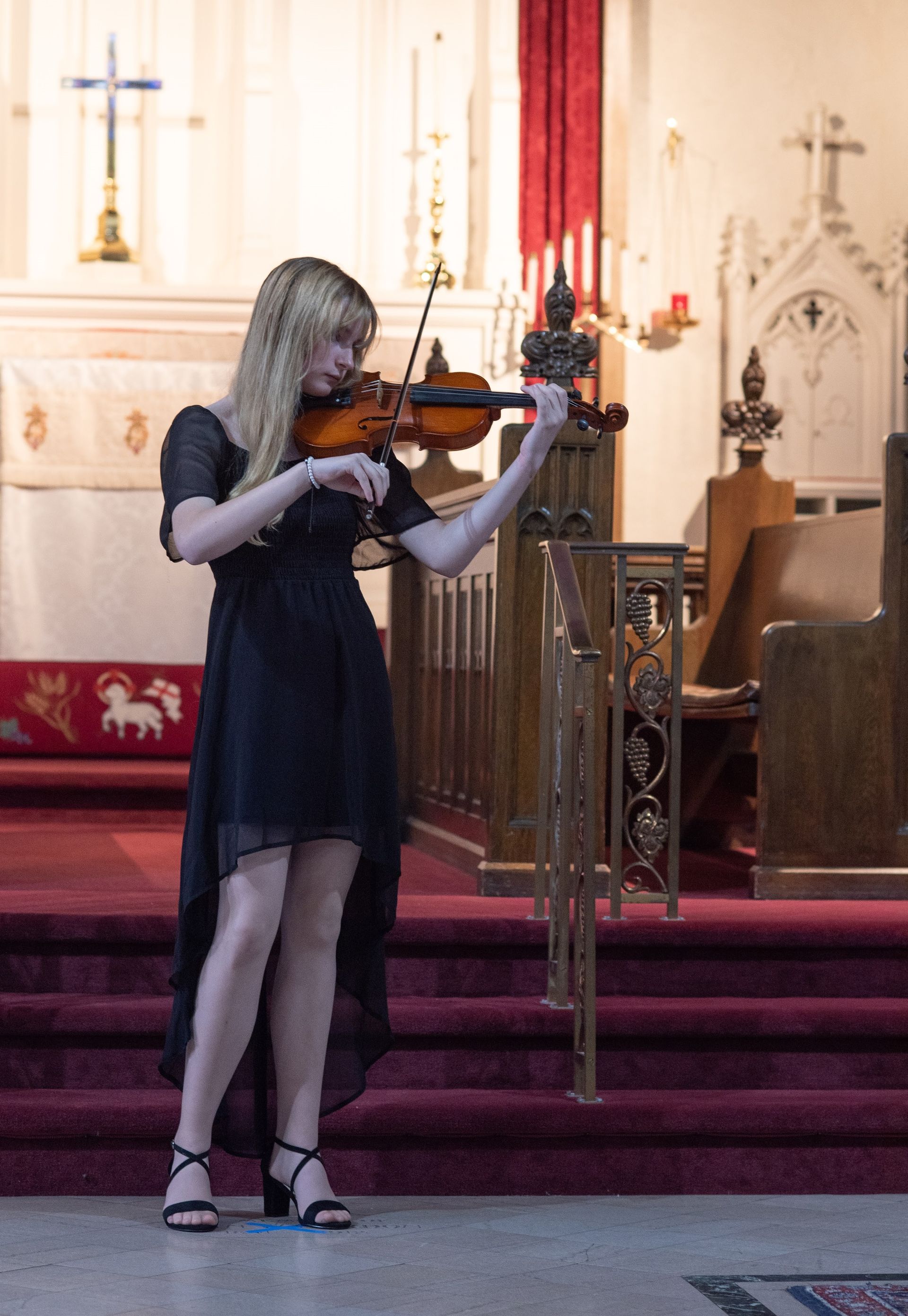 A little girl in a red dress is holding a violin.