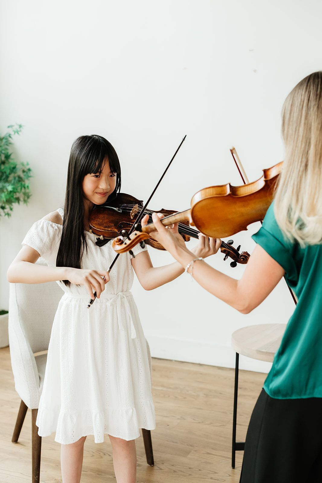 A young girl in a red shirt is playing a violin.