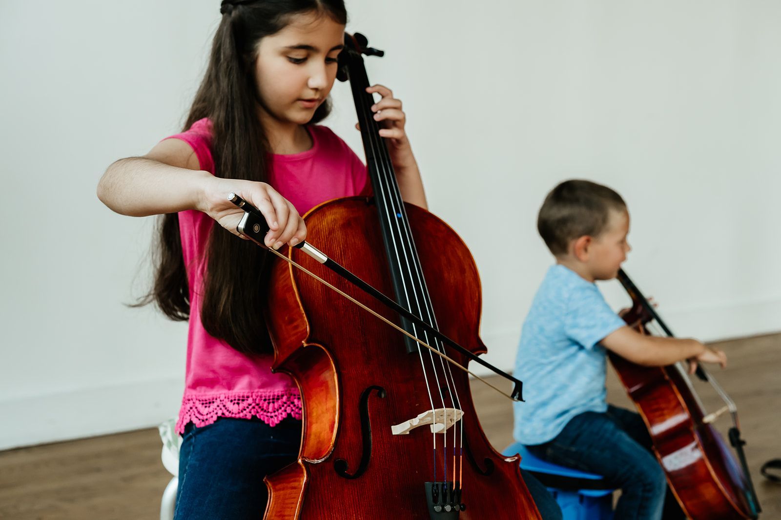 A young boy is playing a cello in front of a purple wall