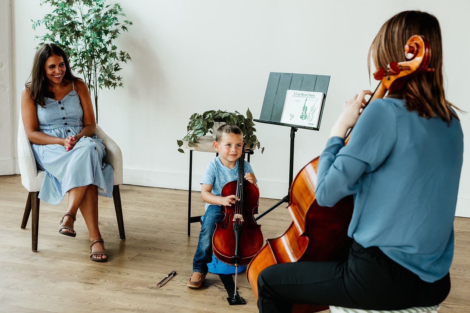 A little boy is learning to play the cello with this teacher and his mom.