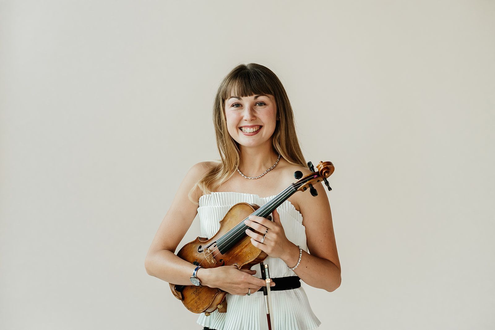 Iuliia Leuck is holding a violin and smiling.