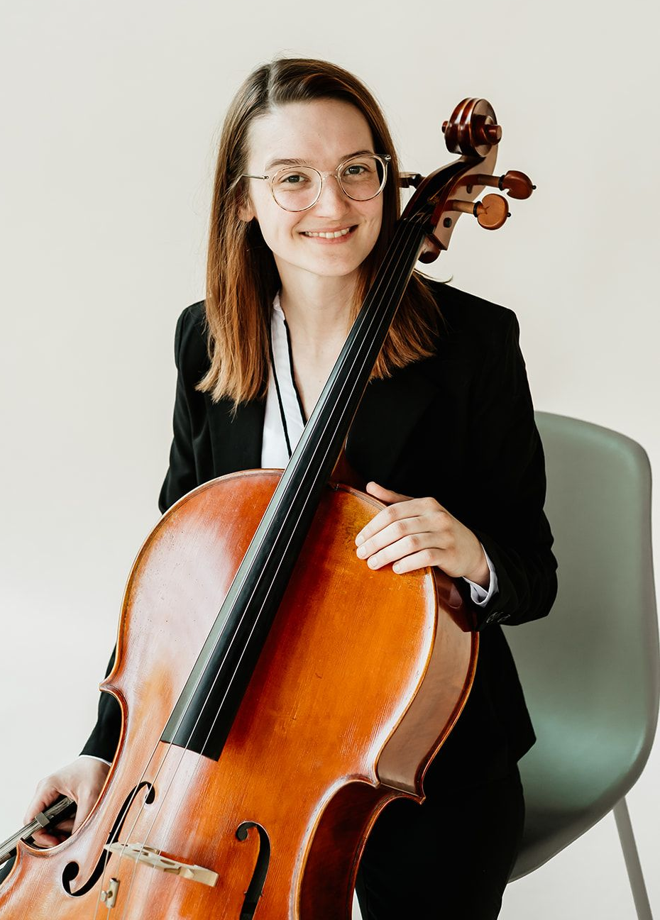 A woman is holding a cello in the woods.