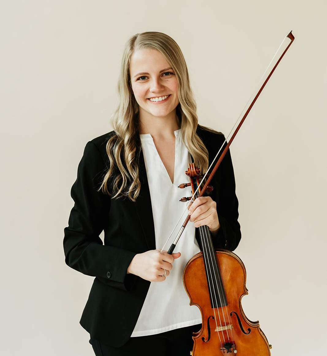 A woman is holding a violin in front of a window.