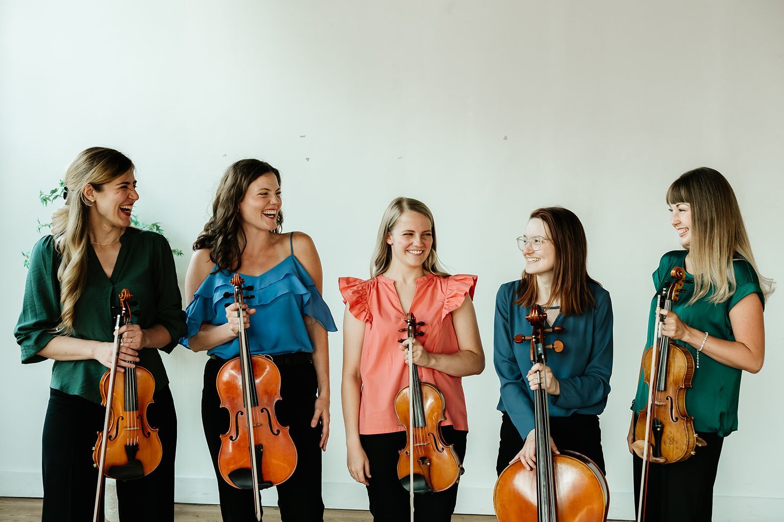 A group of people standing next to each other holding violins and cello.