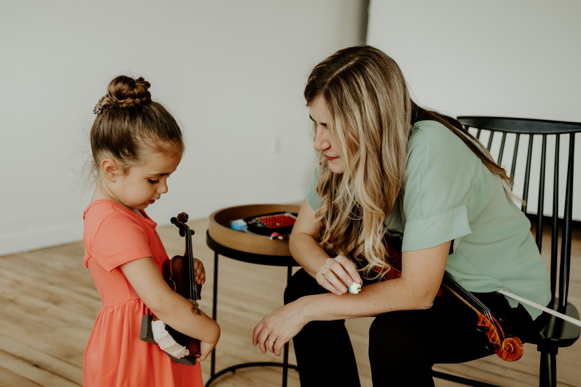 A woman is teaching a little girl how to play a violin.