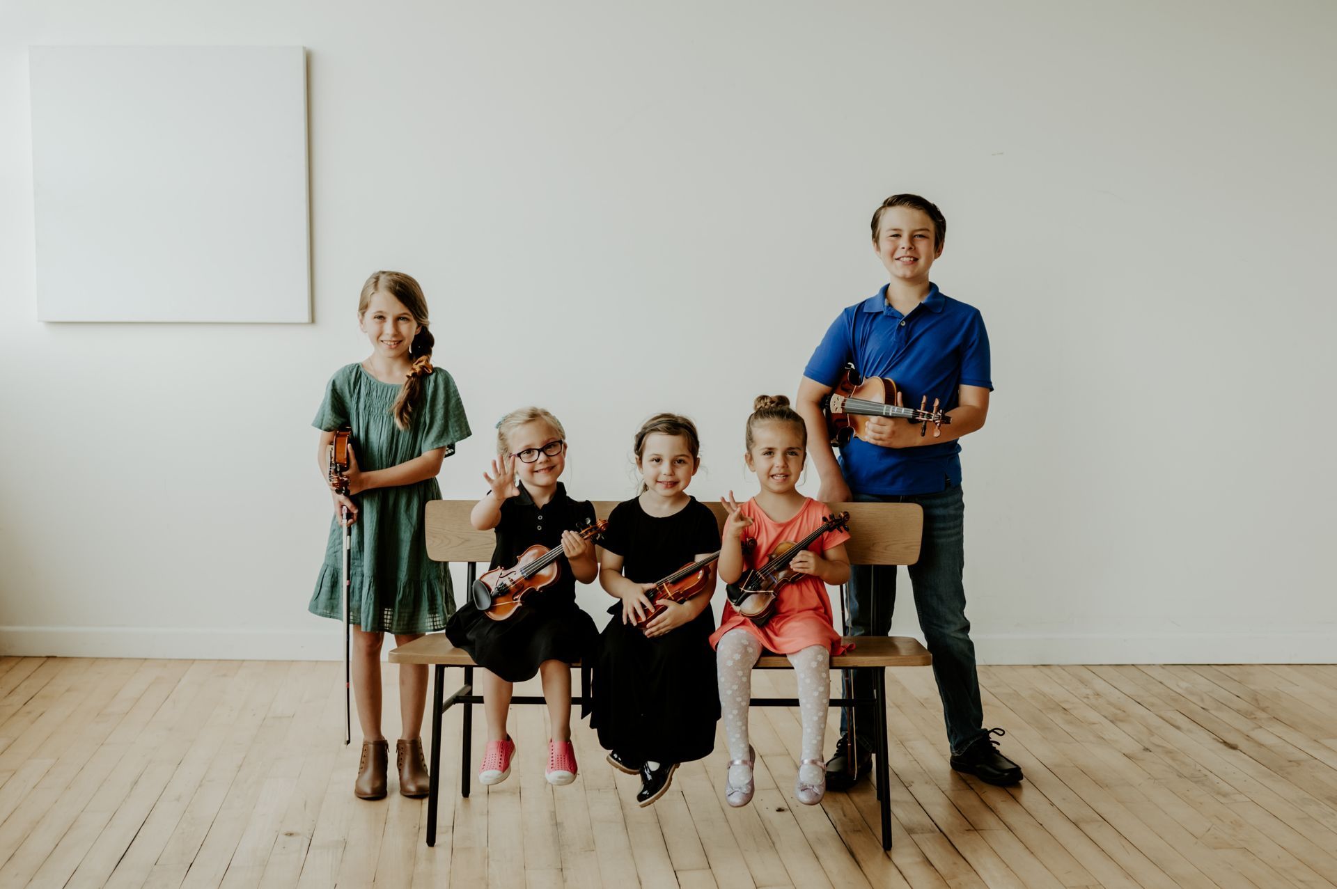 Three little girls are sitting on a bench holding violins.