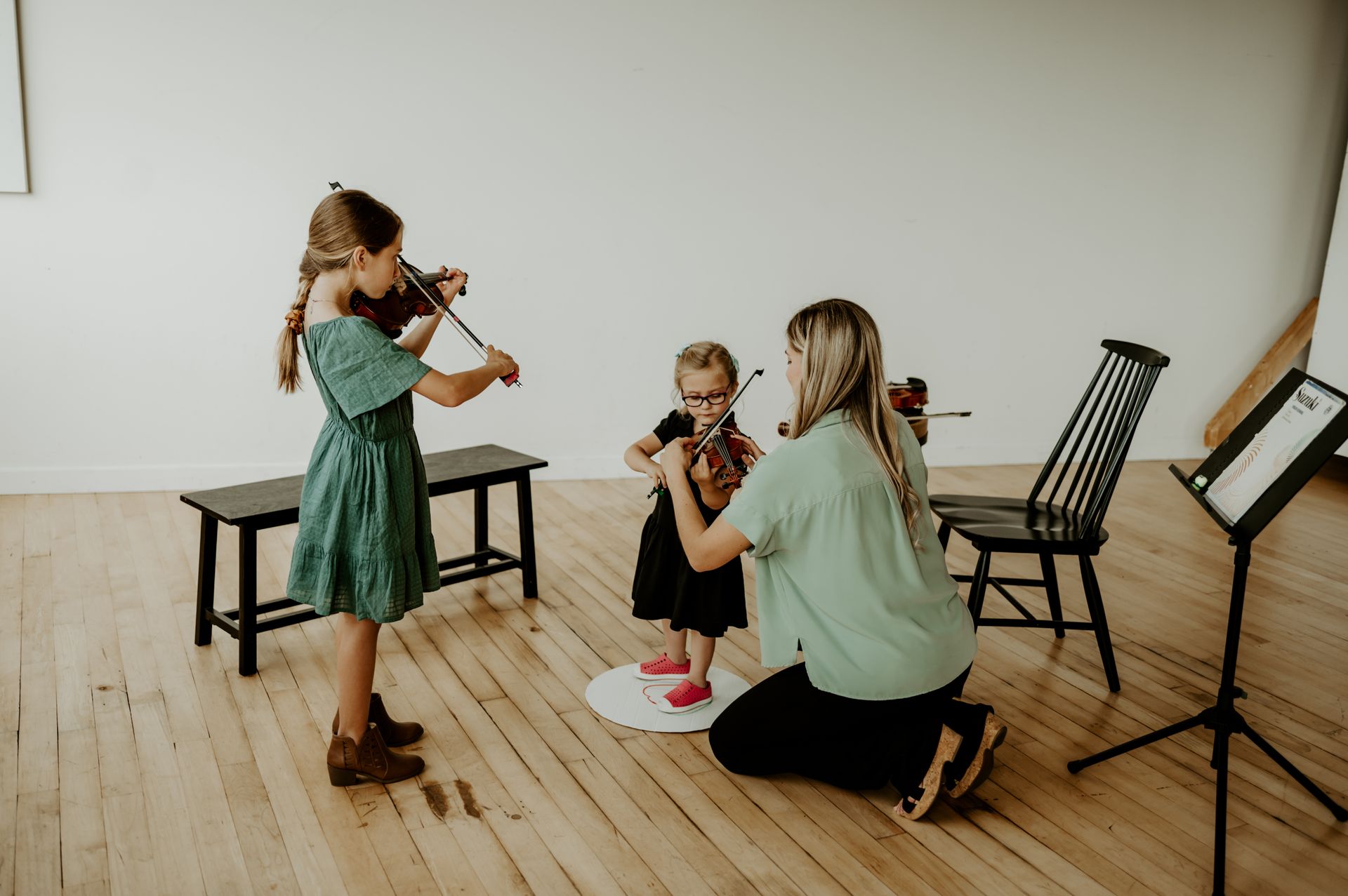 A woman is teaching two young girls how to play violins.