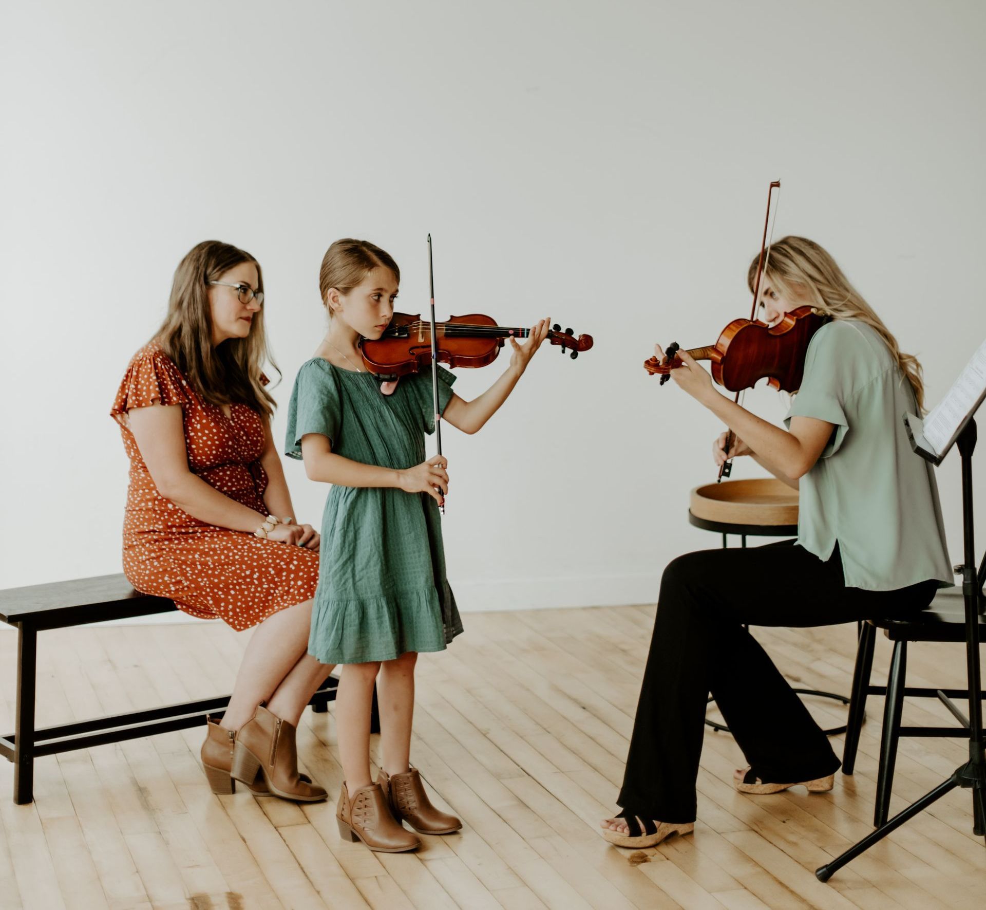 A woman is teaching two young girls how to play violins.