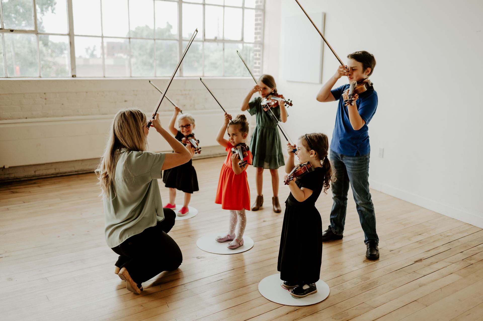 A group of children are playing violins in a room with a teacher.