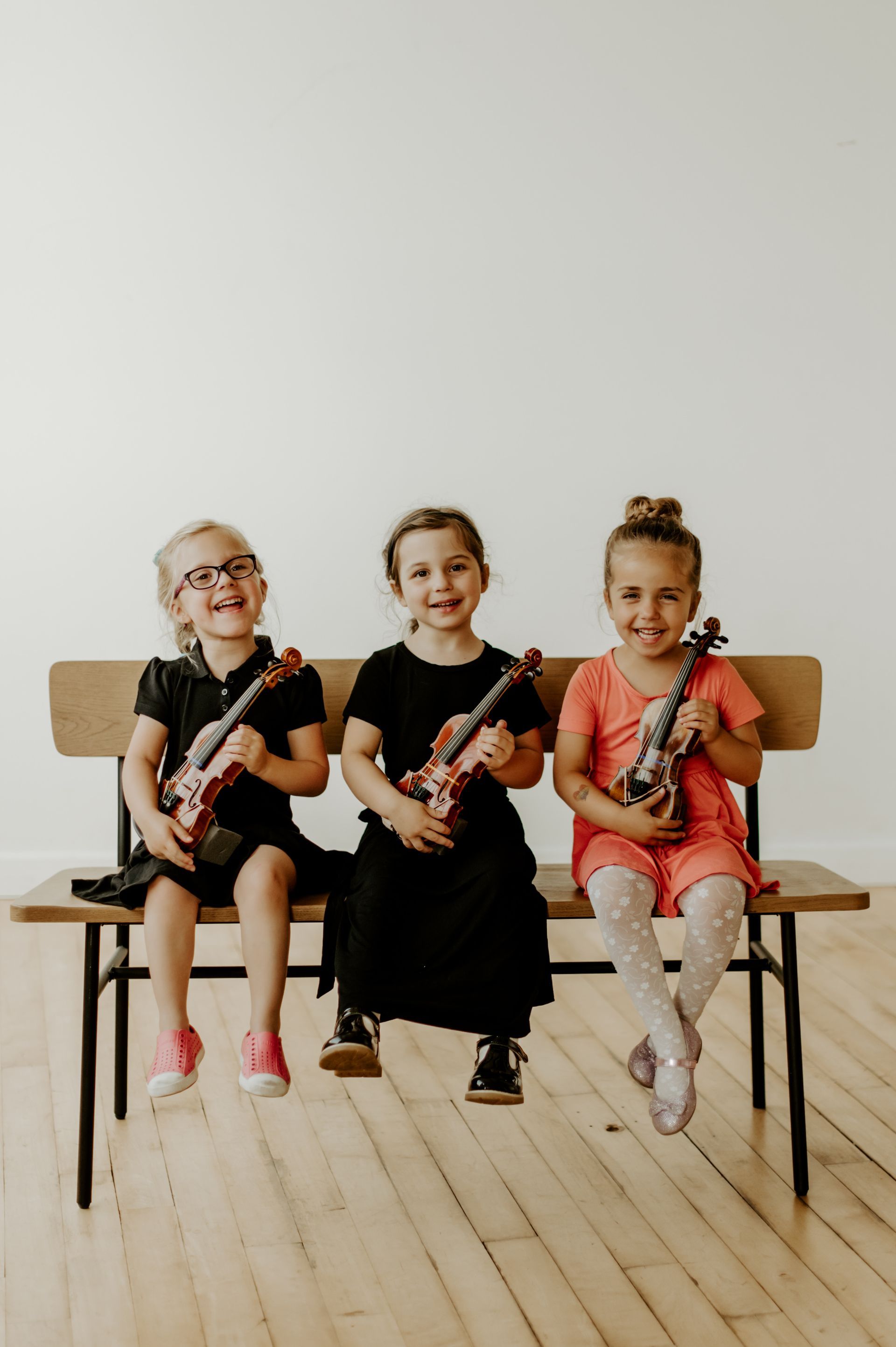 Three little girls are sitting on a bench holding violins.