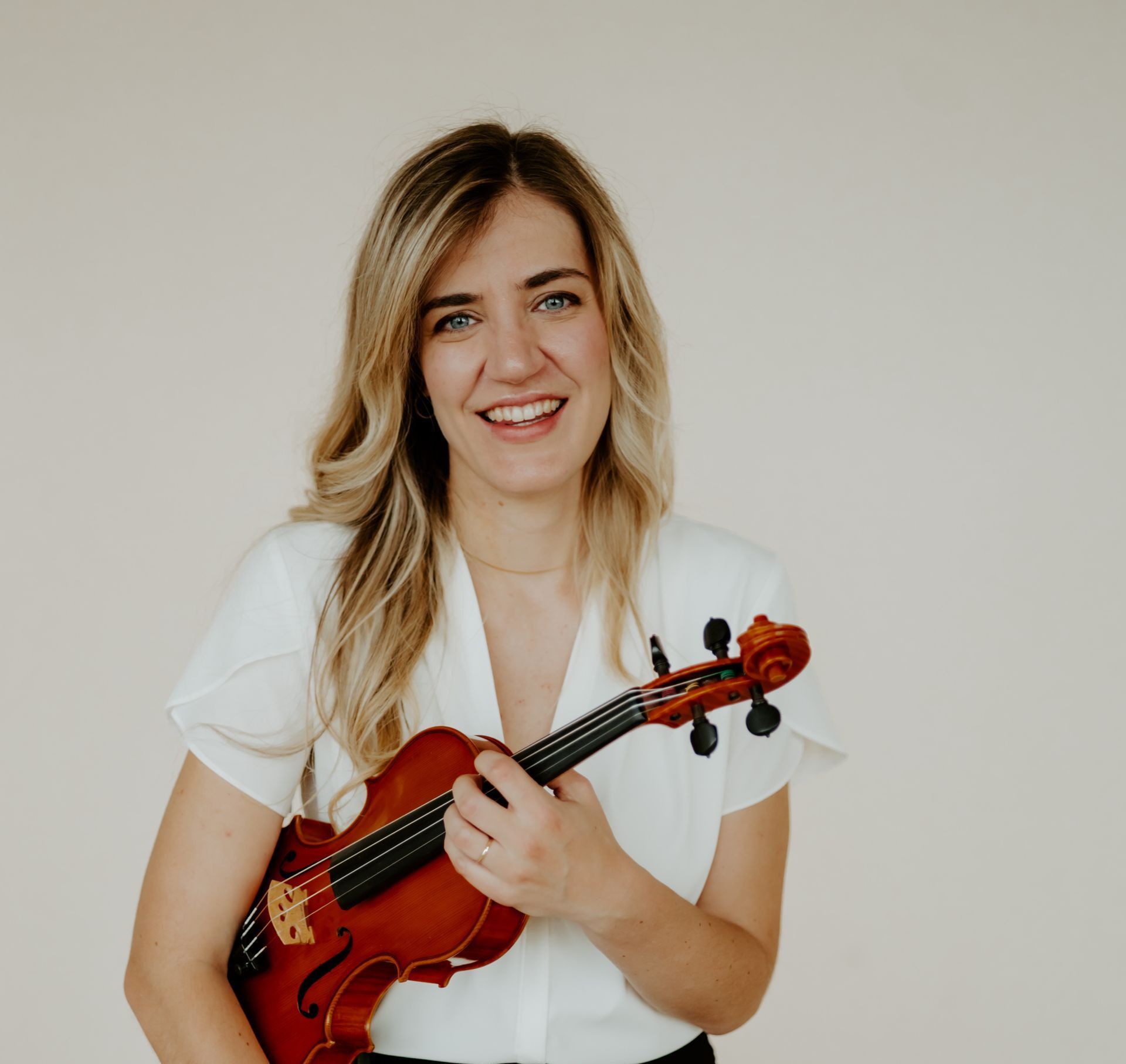 A woman in a white tank top is holding a violin and smiling.