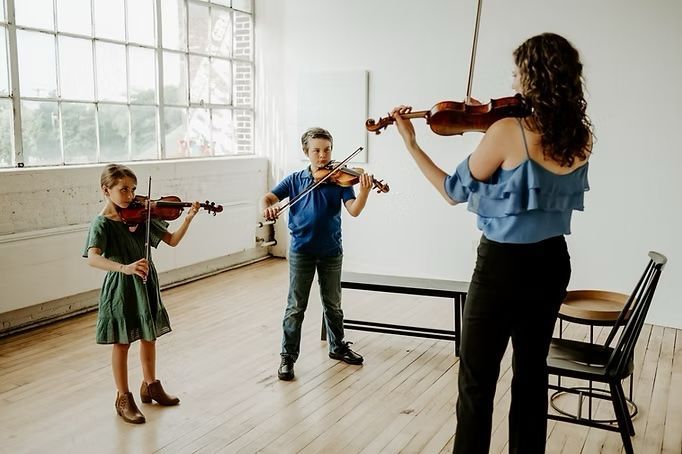 A woman is teaching two children how to play violins in a room.