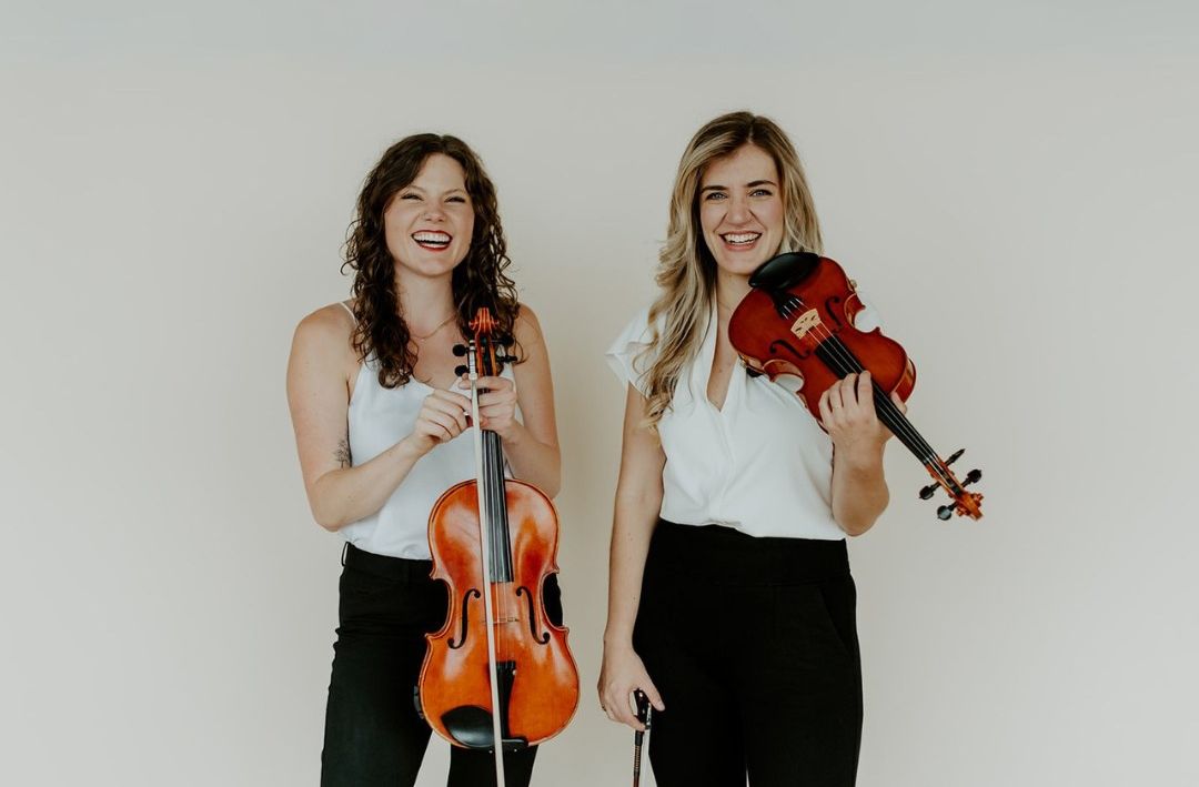 Two women are standing next to each other holding violins.