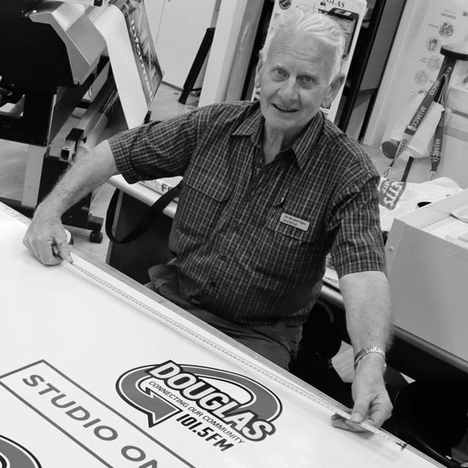 A Man Is Sitting In Front Of A Sign That Says Douglas 100.5 Fm— Quality Printing In Port Douglas, QLD