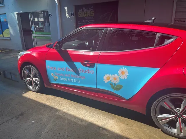 A red car with flowers on the side is parked in front of a building- Sponsorship Signage in Port Douglas, QLD