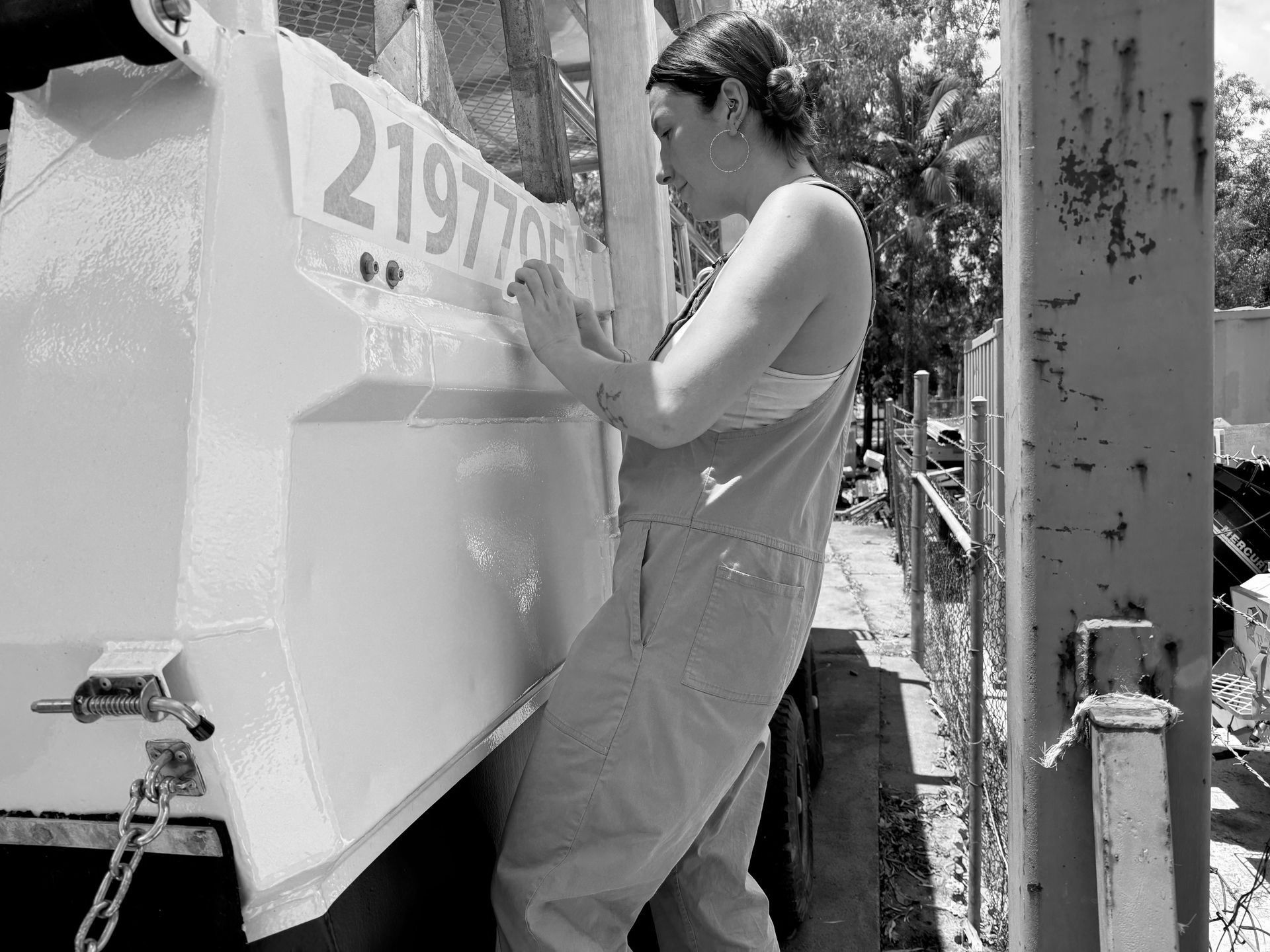 A black and white photo of a woman writing on a sign that says — Quality Printing In Port Douglas, QLD