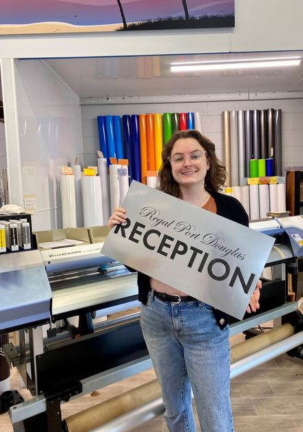 A woman is holding a sign that says reception in a store- Sponsorship Signage in Port Douglas, QLD