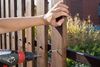 A hand holds a vertical wooden fence board steady as a power drill secures it to a horizontal metal support rail.