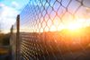 A chain-link fence stands in the foreground against a bright, golden sunrise or sunset.