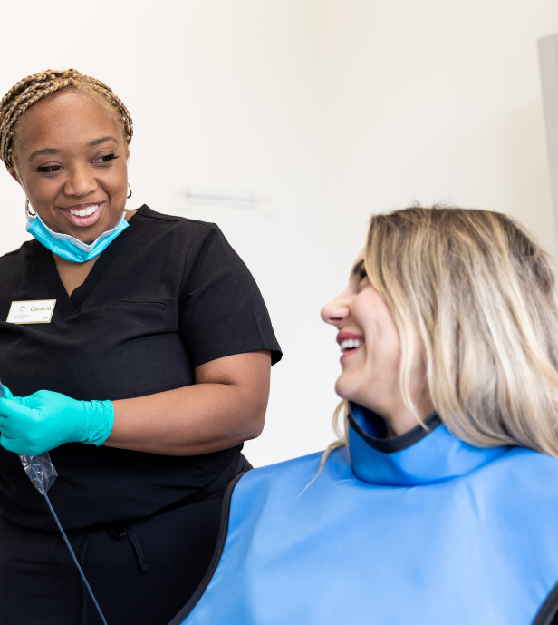 Oasis Wellness Dentistry, Staff smiling at a patient wearing a blue bib in a dental office.