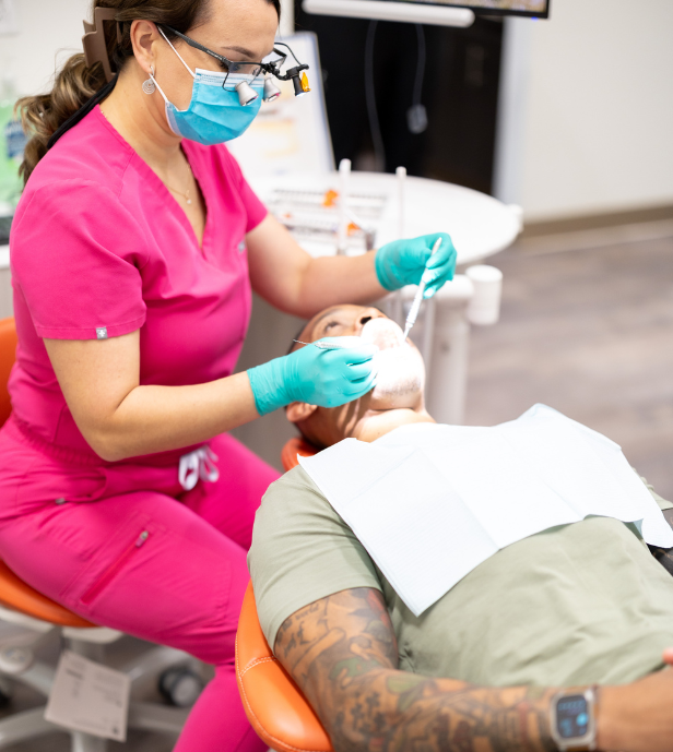 Dr. Shuba at Oasis Wellness Dentistry examining a patient's teeth. They are in a dental chair, inside a dental office.