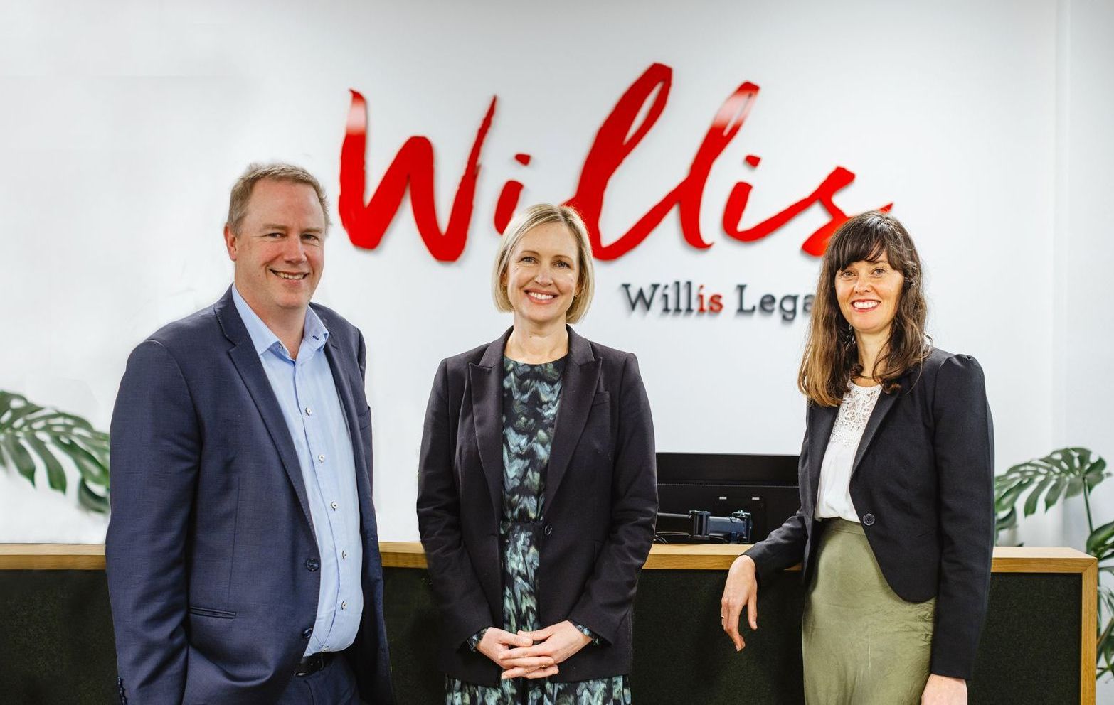 A man and two women are standing in front of a sign that says willis.