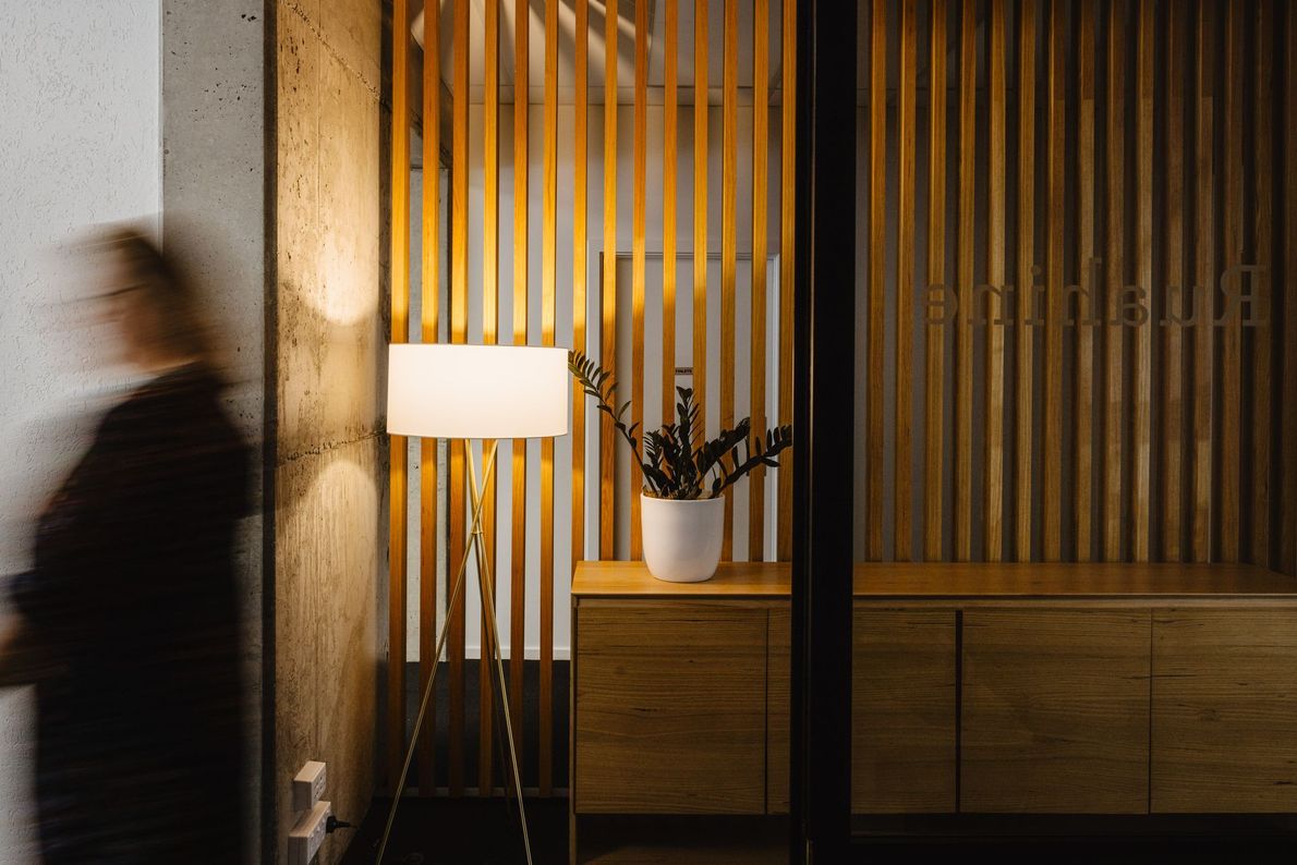 A woman is walking in a room with a lamp and a plant.