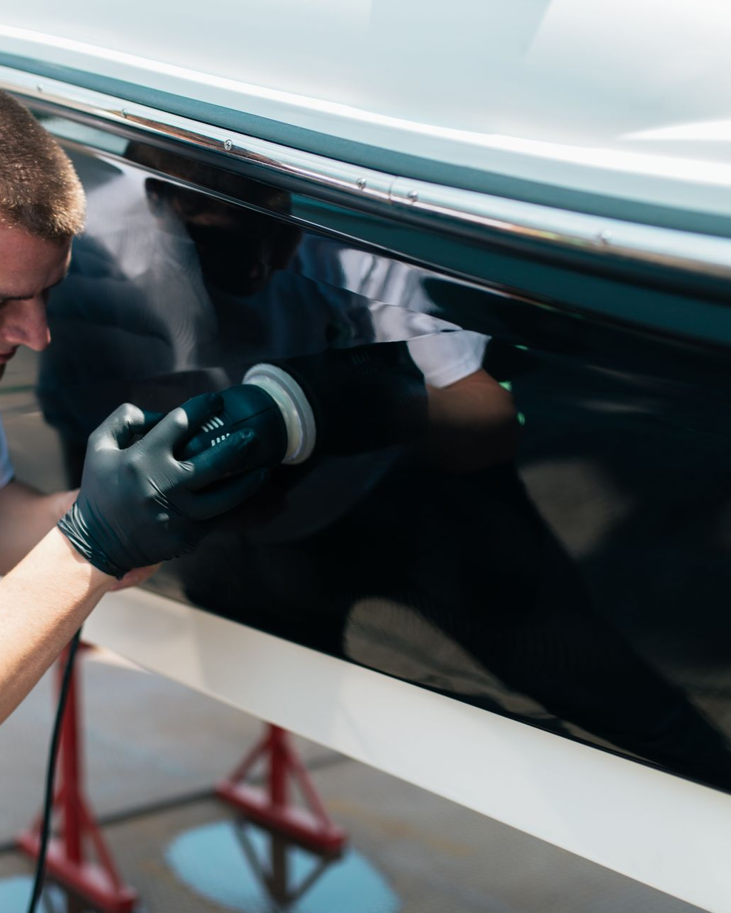 A person wearing black gloves is polishing a black car