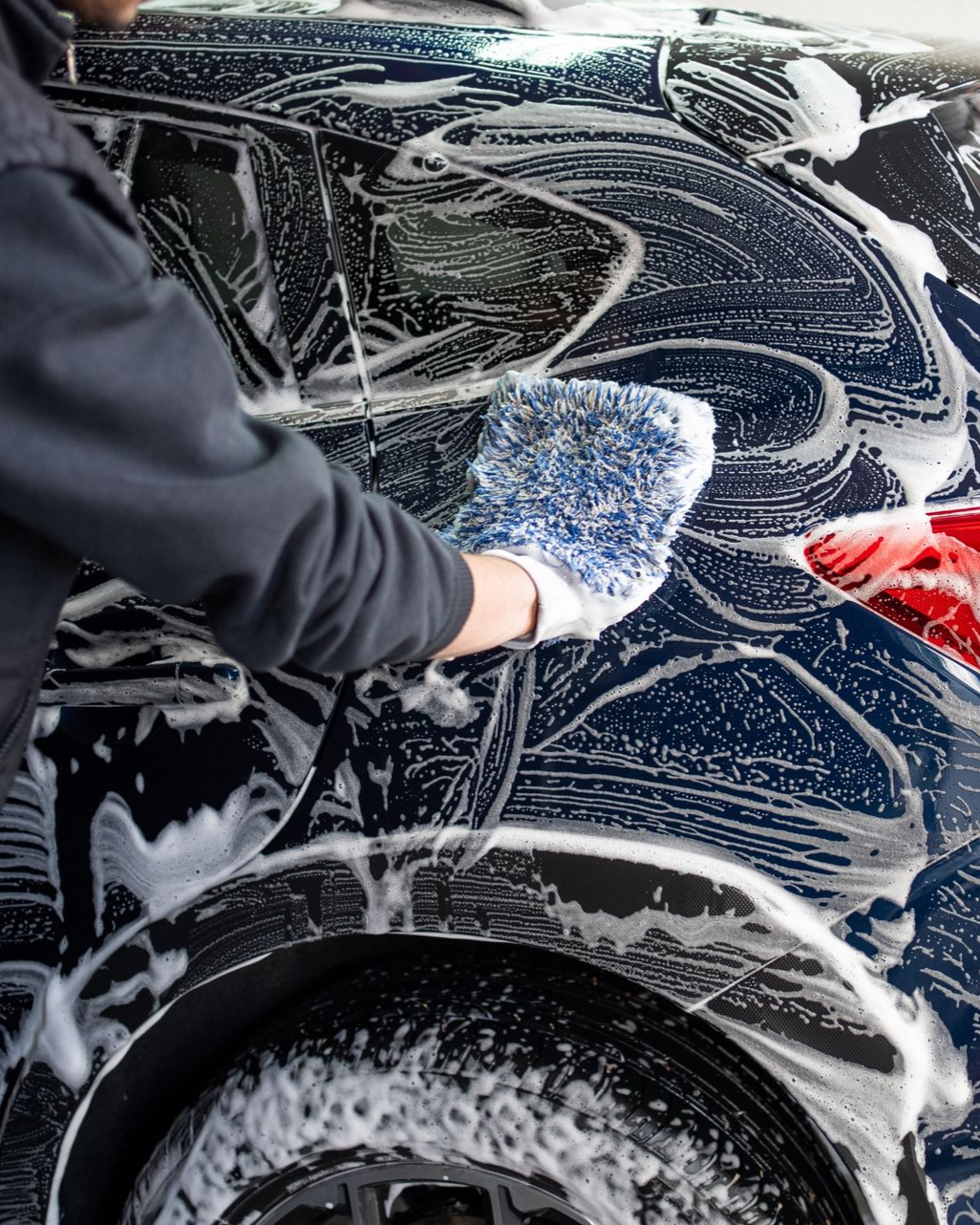 Person washing a dark blue car with a soapy mitt.