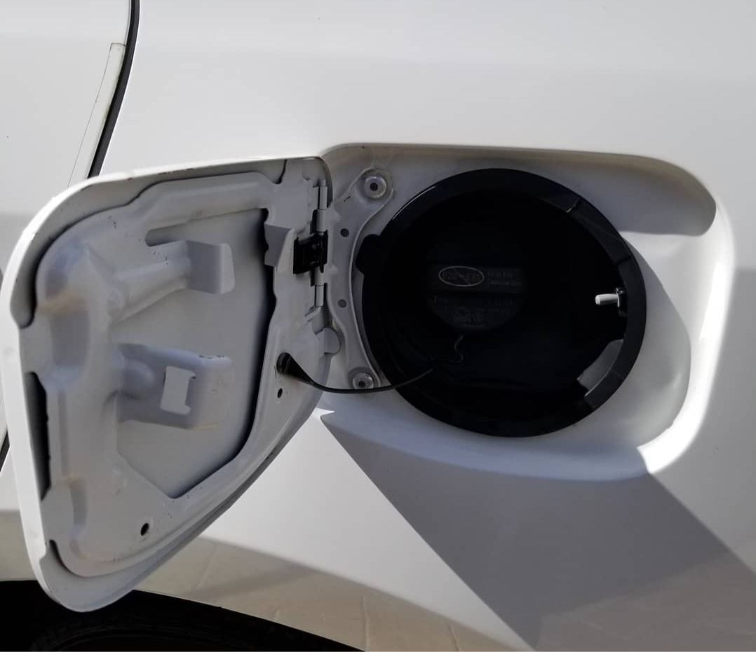 Open white car gas tank door revealing a black fuel cap.