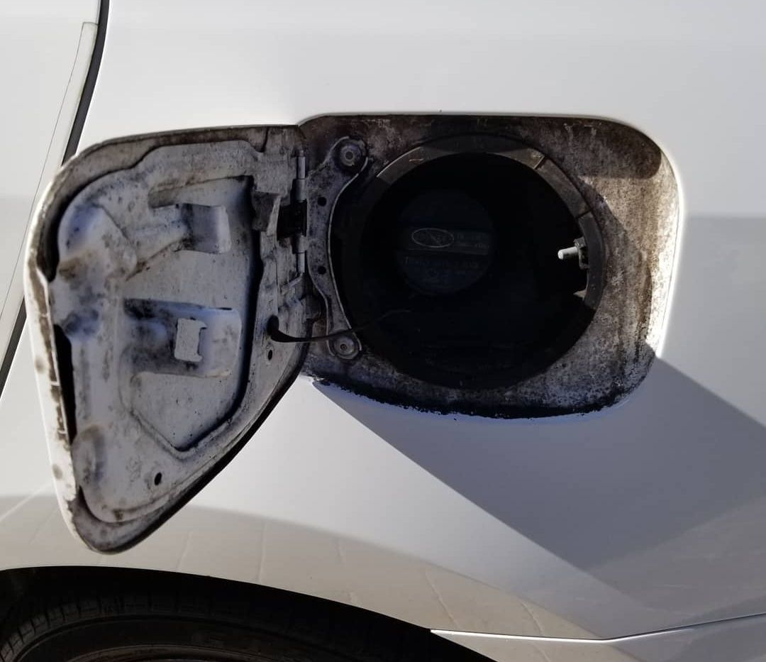 Open white car fuel door revealing the gas cap.