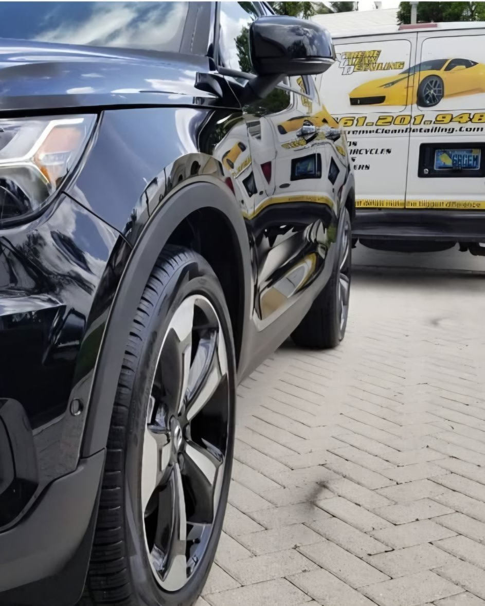 A person wearing black gloves is polishing the hood of a red car.