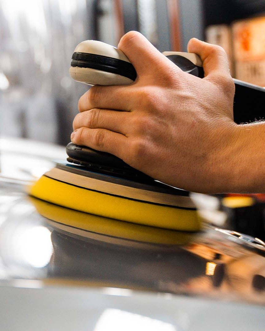 A person is cleaning a blue car with an orange towel