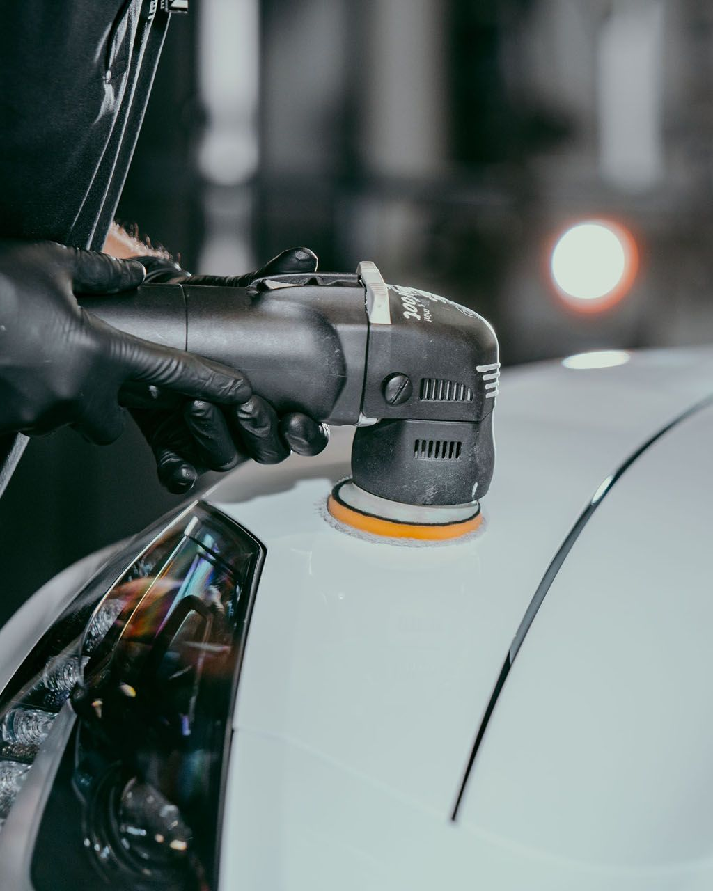 A person wearing black gloves is polishing a black car