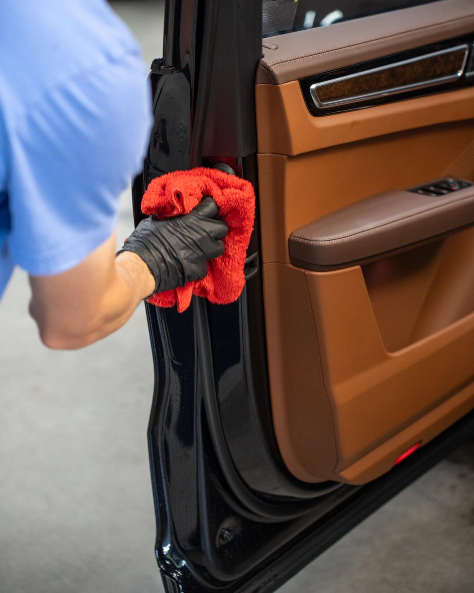 Person in black glove cleaning car door frame with a red cloth.
