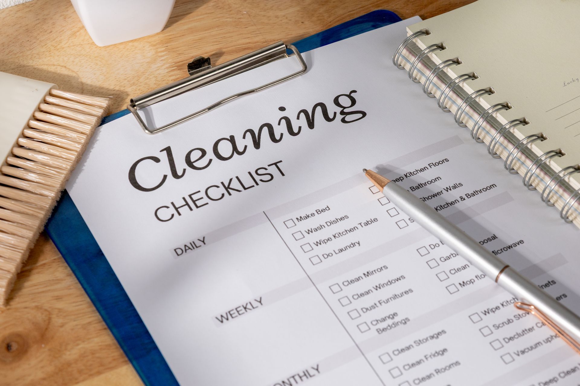 Cleaning supplies on a table: spray bottles, gloves, sponges, and a basket, with a blurred kitchen background.