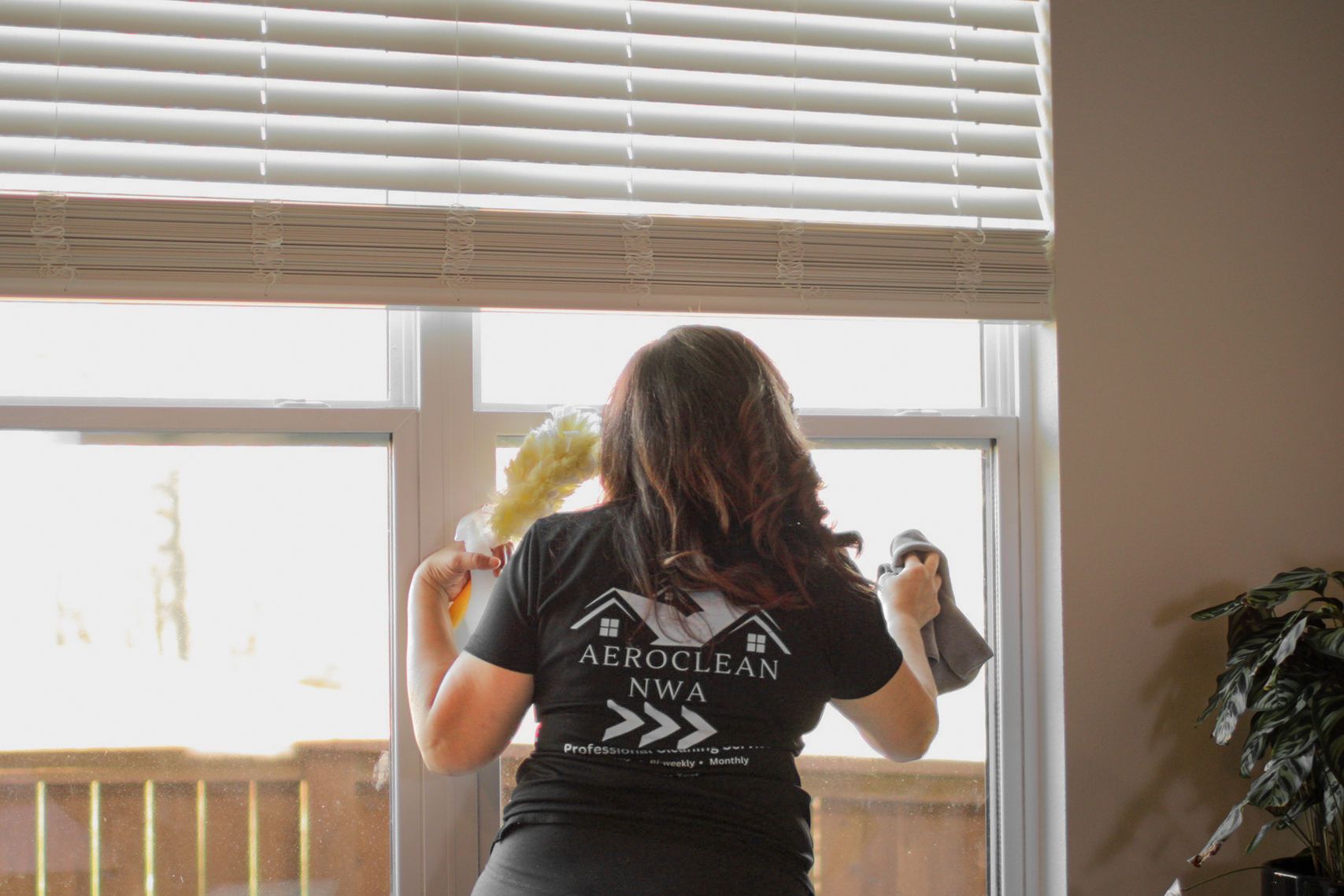 Woman cleaning a window, holding cloths, with a company logo shirt.