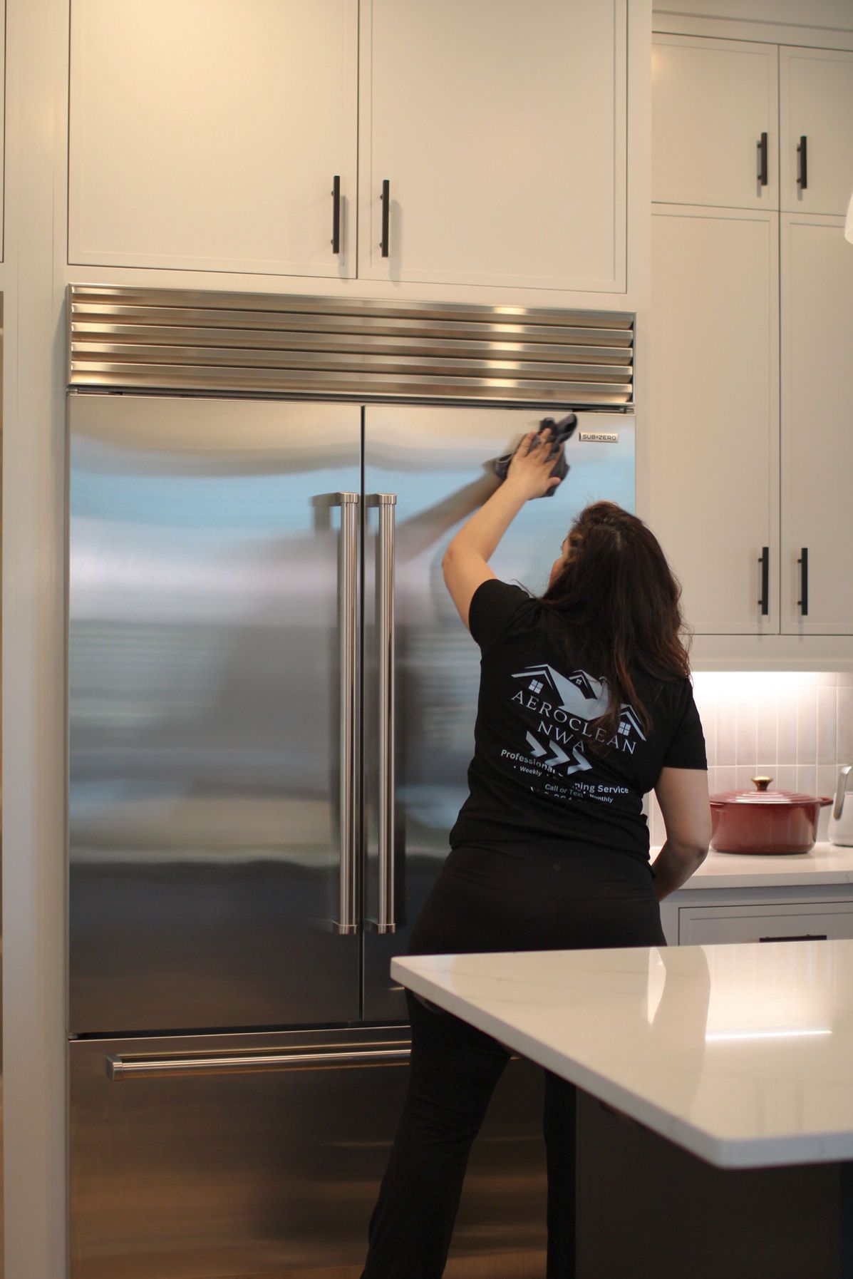 Person standing in a kitchen reaches toward the top of a large refrigerator.