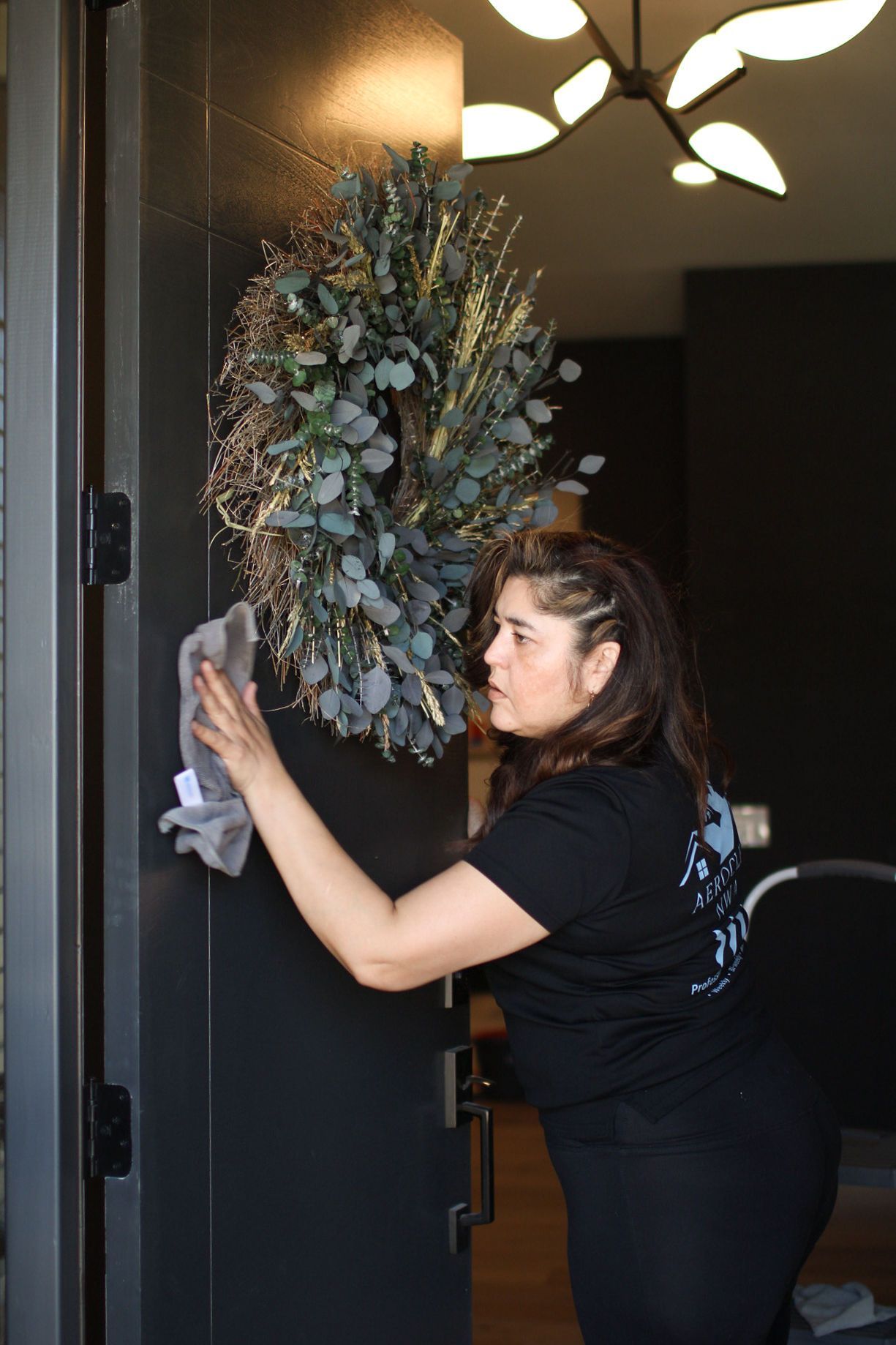 Woman wiping front door with a cloth, wreath on door.