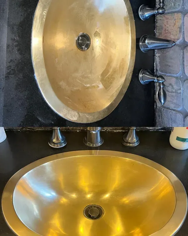 Two gold-colored oval sinks with brushed metal faucets mounted on a black countertop and backsplash.