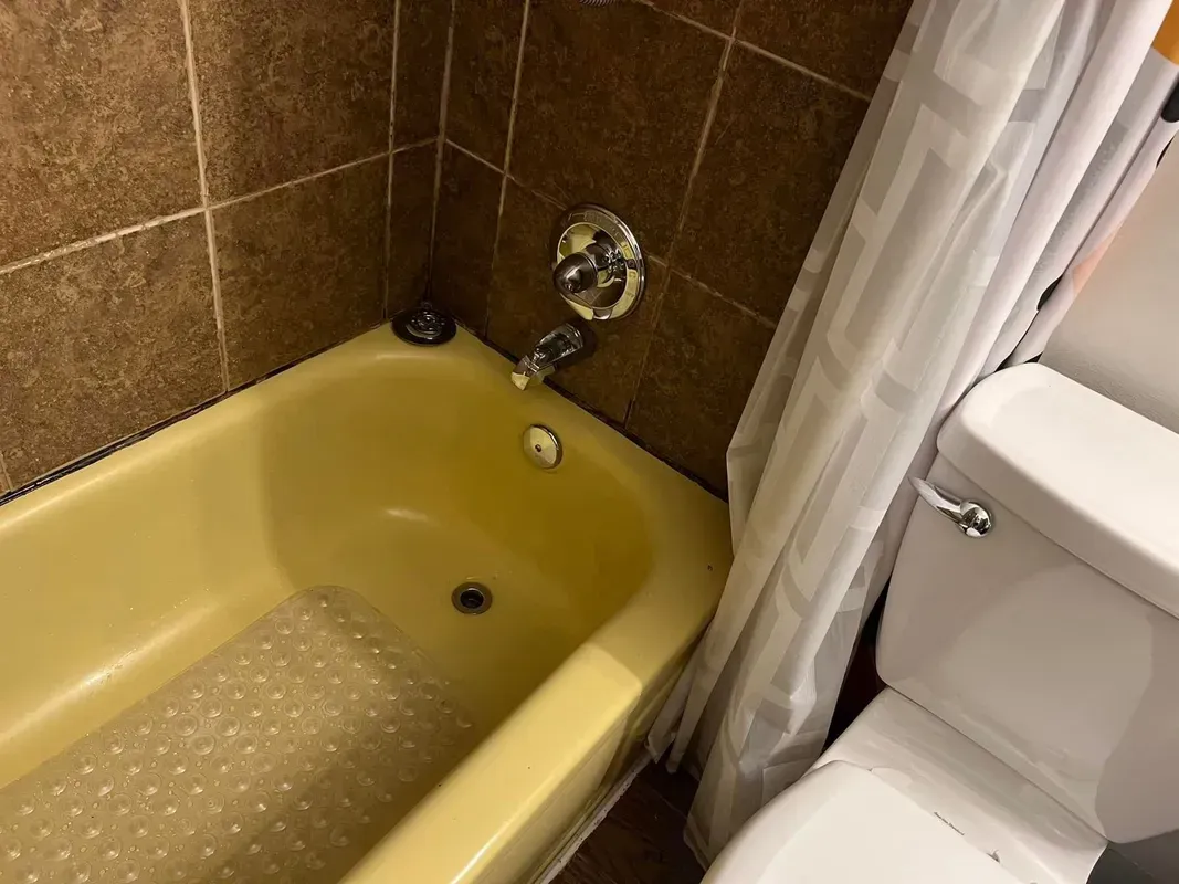 Yellow bathtub, tile walls, chrome faucet, white toilet with shower curtain to the right.