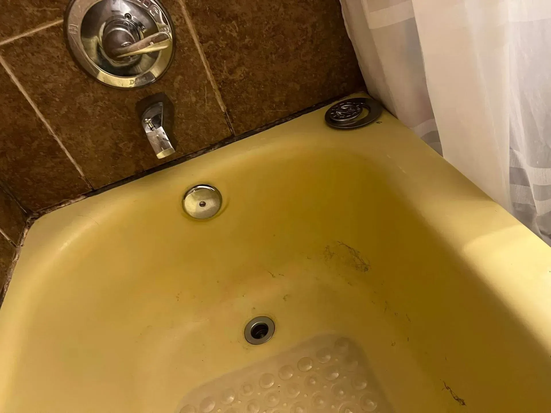 Yellow bathtub with chrome fixtures; brown tiled wall.