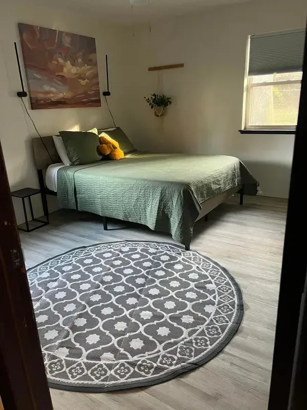 Bedroom with a green quilt, art, and a round gray patterned rug.