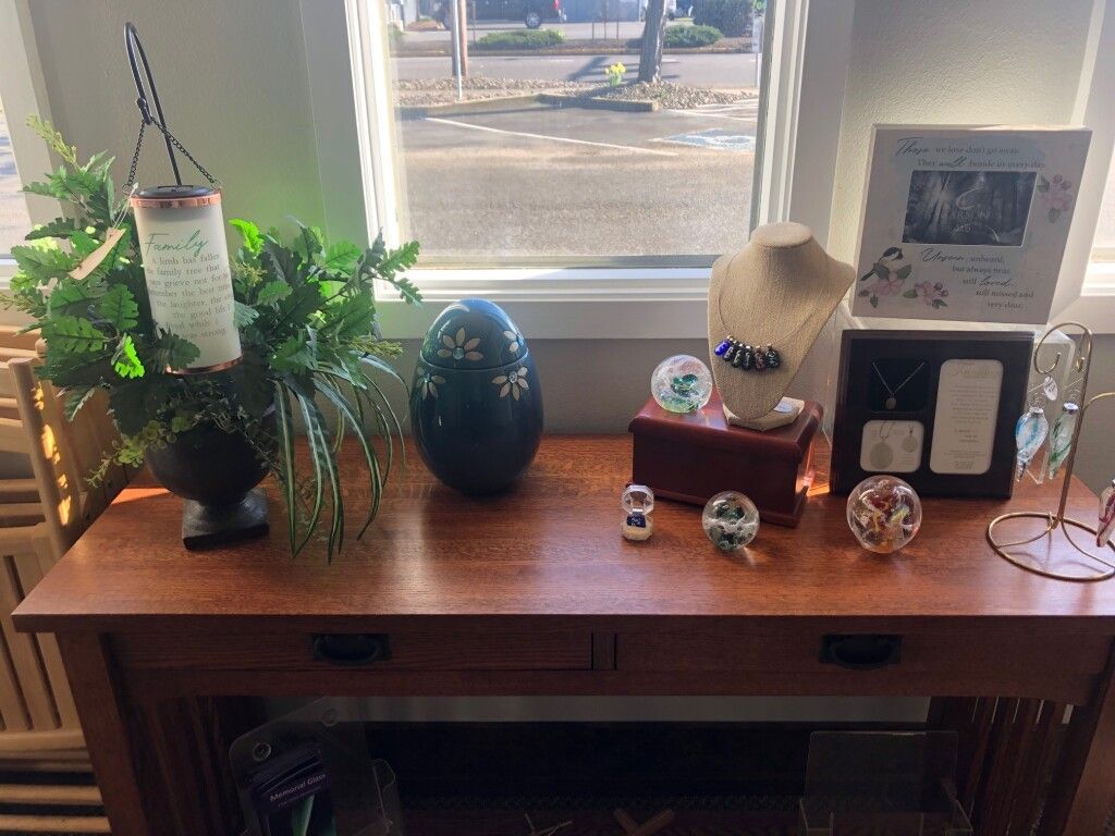 Wooden table with decorative items displayed in front of a window. Includes greenery, jewelry, and framed pictures.