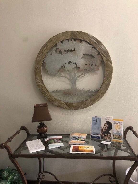 A framed tree art above a table with brochures and a lamp.